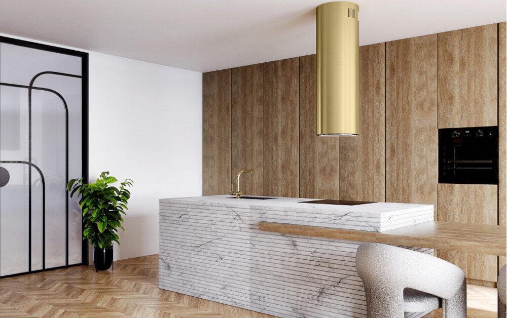 Okap GLOBALO Heweno Isola 39.2 Złoty mat Na zdjęciu przedstawiono przestronną kuchnię w minimalistycznym stylu, z centralnie umieszczoną wyspą wykonaną z jasnego, marmurowego kamienia. Nad wyspą zawieszony jest efektowny, złoty okap cylindryczny, który stanowi designerski akcent wnętrza. W tle widać wysokie drewniane zabudowy oraz czarny piekarnik w zabudowie, a całość uzupełnia eleganckie krzesło i zielona roślina w doniczce szerokość 39 cm timer czas Głośność 69 db
