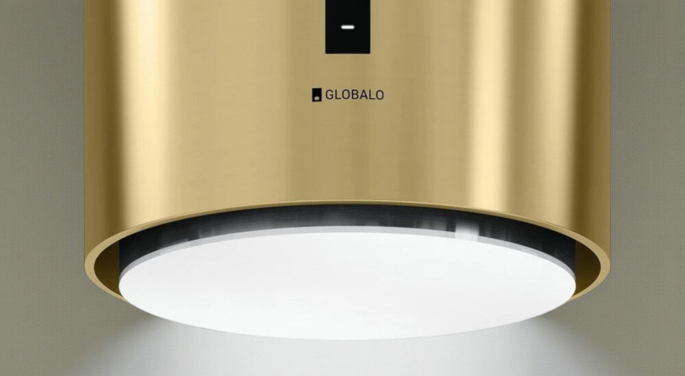 Okap GLOBALO Heweno Isola 39.2 Złoty mat Zdjęcie przedstawia zbliżenie na dolną część cylindrycznego, złotego okapu kuchennego marki GLOBALO, z wyraźnie widocznym, okrągłym panelem LED odpowiadającym za równomierne, jasne oświetlenie powierzchni roboczej. Widoczny jest minimalistyczny design oraz dotykowy panel sterowania oświetlenie led naturalne światło komfort gotowania widoczność w kuchni gotowanie wieczorne energooszczędne oświetlenie led okap oświetlenie kuchenne