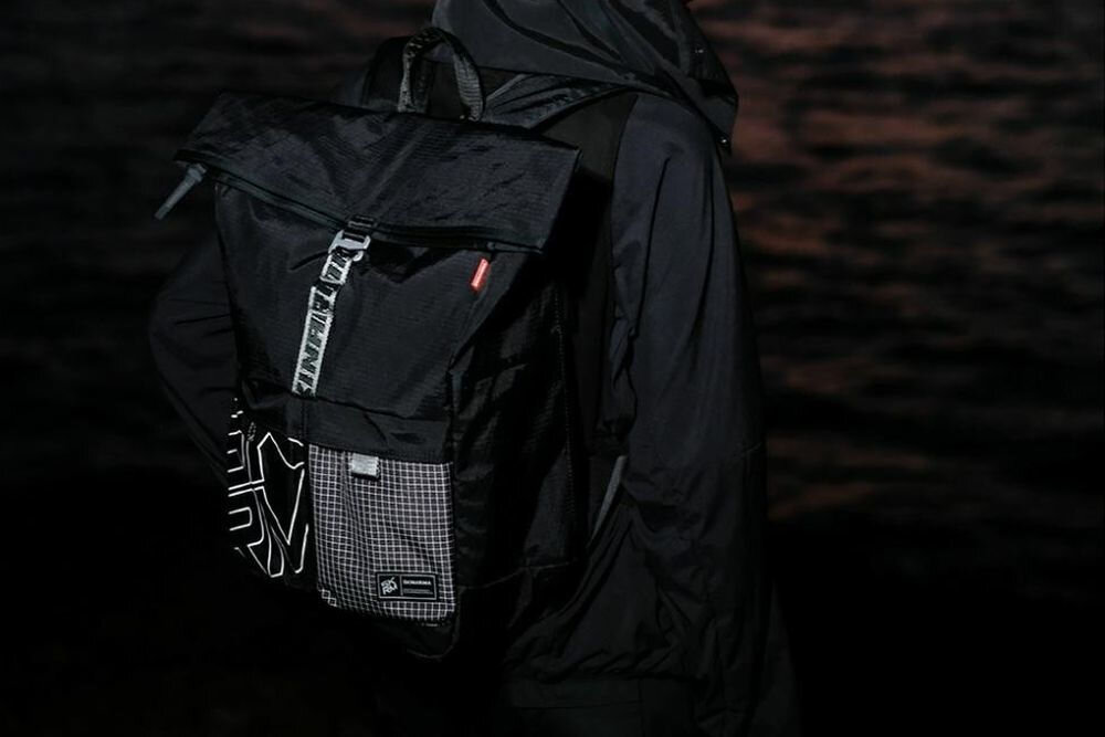 Plecak SKINARMA Jager Brązowy prezentacja plecaka założonego na plecach ciemne tło komora główna i kieszenie boczne wodoodporny nylon ripstop laptop do 14 cali kieszonka siateczkowa zamek boczny przestrzeń na drobiazgi