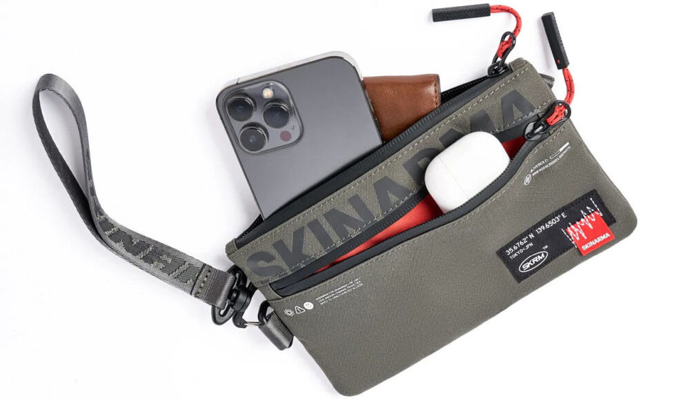 Torebka na telefon SKINARMA Fardel Oliwkowy prezentacja torebki na białym tle z wystającym telefonem portfelem i słuchawkami z kieszeni wnętrze z kieszeniami i wodoodporny materiał ułatwienie organizacji