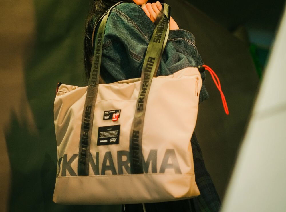 Torba SKINARMA Fardel Kość słoniowa prezentacja torby trzymanej przez osobę na rozmazanym tle