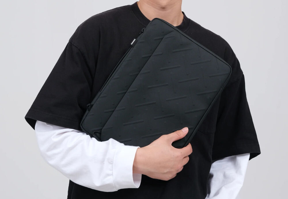 Torba na laptopa SKINARMA Juno 14 cali Zielony torba trzymana w dłoni przy ciele przez osobę na szarym tle wodoodporny nylon o wytłaczanej strukturze ochrona laptopa przed wilgocią kurzem i zarysowaniami do 14 cali praktyczność