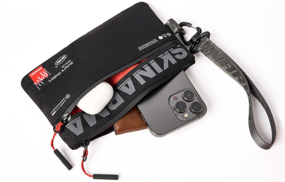 Torebka na telefon SKINARMA Fardel Czarny prezentacja torebki na białym tle z wystającym telefonem portfelem i słuchawkami z kieszeni wnętrze z kieszeniami i wodoodporny materiał ułatwienie organizacji