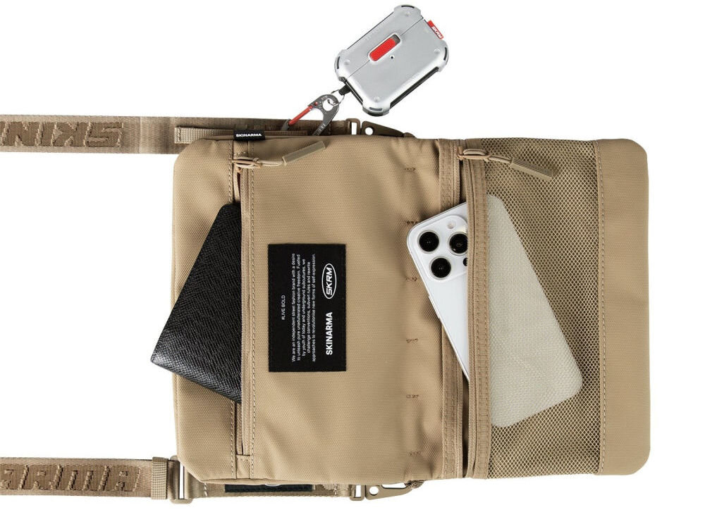 Torebka Crossbody SKINARMA Juno Khaki prezentacja torebki na białym tle z wystającym telefonem i portfelem z kieszeni wnętrze i pasek SCOUT XE magnetyczne zapięcie odporna na zachlapania nylon tłoczony wzór kieszeń z siatki