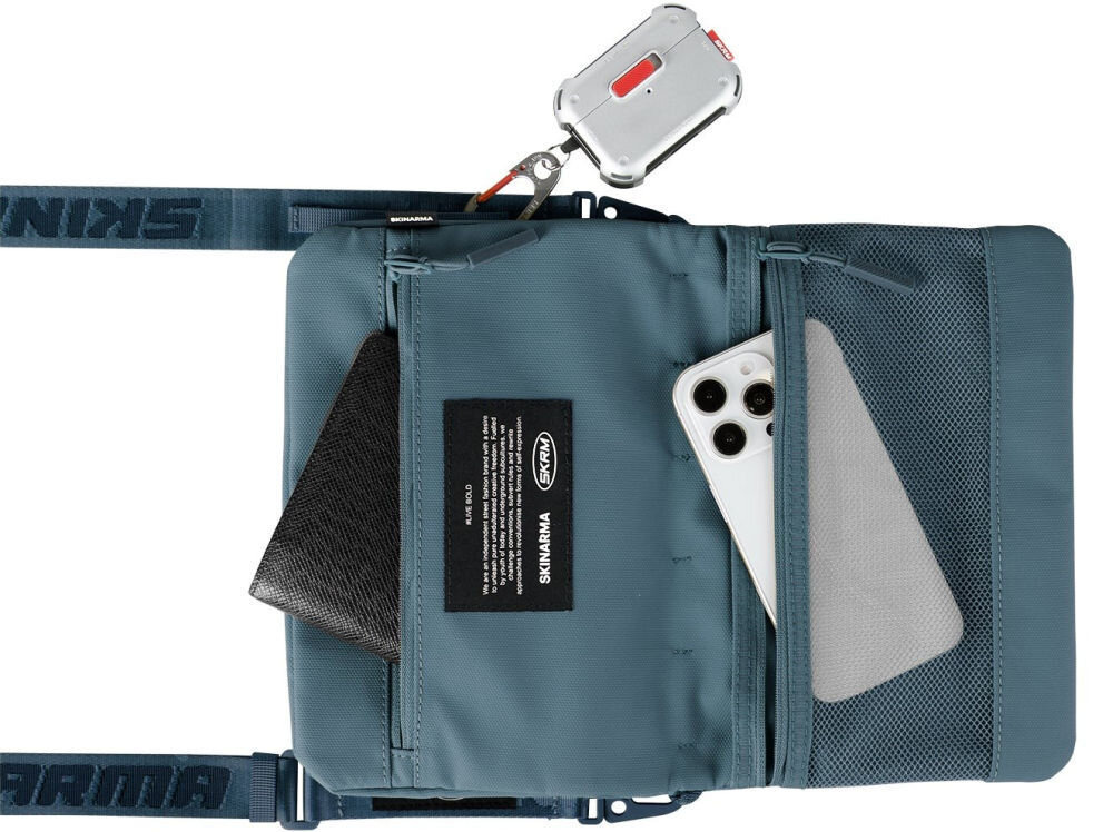 Torebka Crossbody SKINARMA Juno Niebieska prezentacja torebki na białym tle z wystającym telefonem i portfelem z kieszeni wnętrze i pasek SCOUT XE magnetyczne zapięcie odporna na zachlapania nylon tłoczony wzór kieszeń z siatki