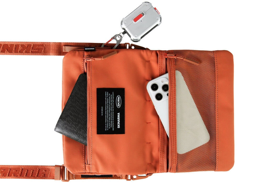 Torebka Crossbody SKINARMA Juno Pomarańczowy prezentacja torebki na białym tle z wystającym telefonem i portfelem z kieszeni wnętrze i pasek SCOUT XE magnetyczne zapięcie odporna na zachlapania nylon tłoczony wzór kieszeń z siatki