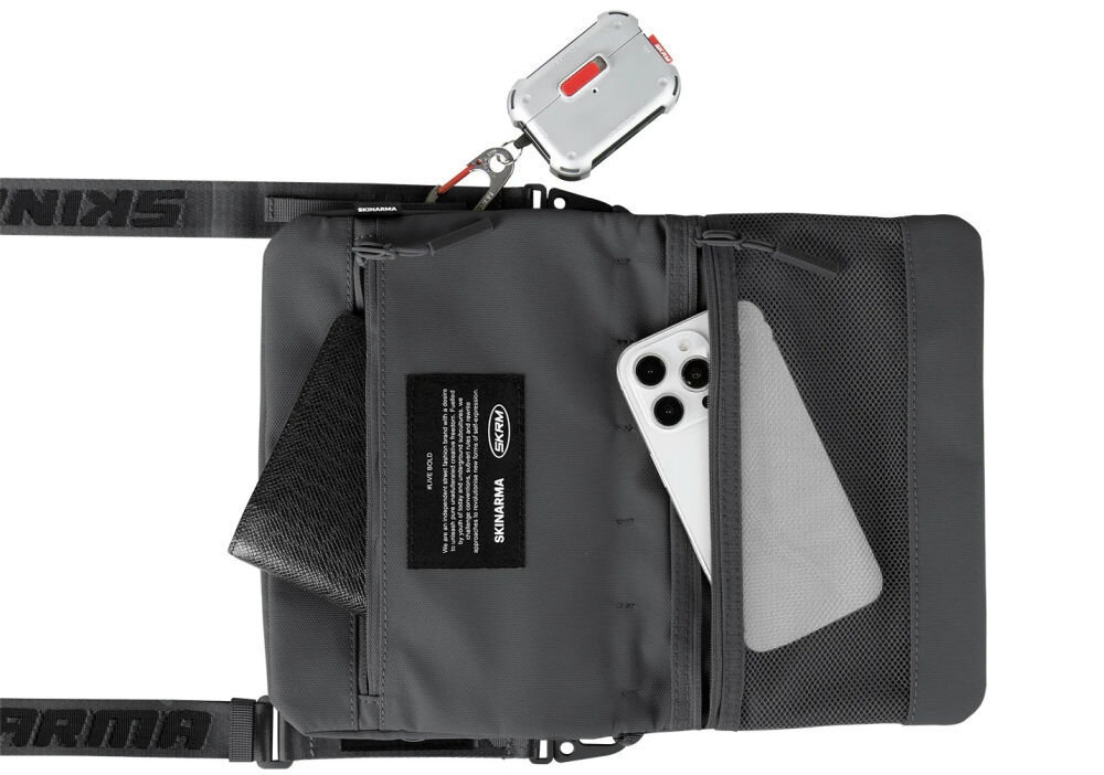 Torebka Crossbody SKINARMA Juno Ciemnoszary prezentacja torebki na białym tle z wystającym telefonem i portfelem z kieszeni wnętrze i pasek SCOUT XE magnetyczne zapięcie odporna na zachlapania nylon tłoczony wzór kieszeń z siatki