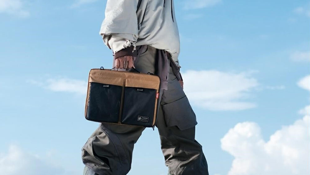 Torba na laptopa SKINARMA Jager 14 cali Brązowy prezentacja torby trzymanej w dłoni przez osobę w tle niebo z chmurami połączenie stylu i technologii