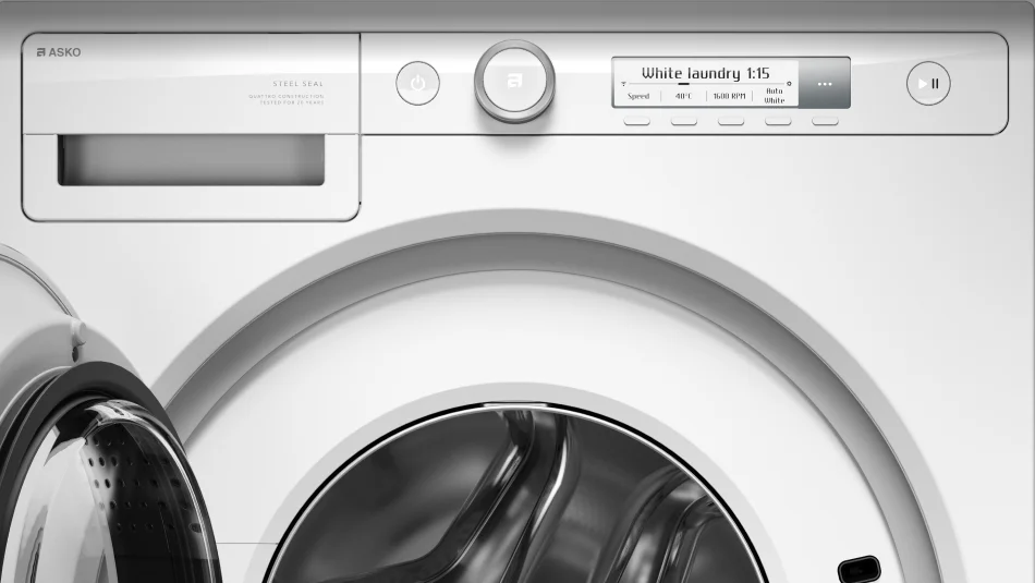 Pralka z widocznym panelem sterowania, na którym wyświetla się tekst \'White laundry 1:15\'. Na urządzeniu widoczne są napisy \'ASKO\', \'STEEL SEAL\', \'QUATTRO CONSTRUCTION\', \'TESTED FOR 20 YEARS\'.