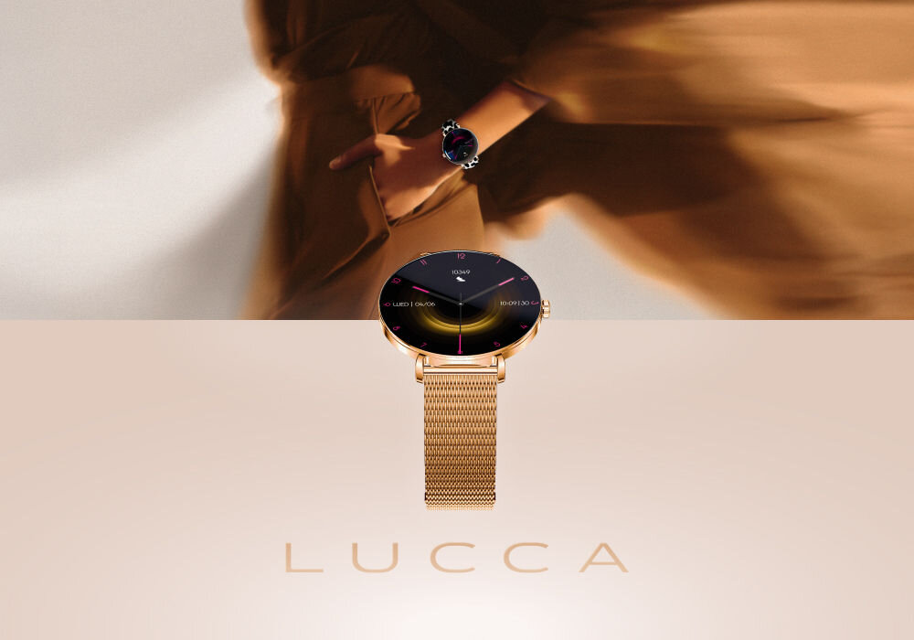 Smartwatch FOREVER SB-370 Lucca Różowe złoto + Pasek łaciaty Smartwatch Lucca w kolorze różowego złota z bransoletą mesh i czarną tarczą, eksponowany na jasnym tle. W tle widać niewyraźną postać kobiety w beżowej odzieży