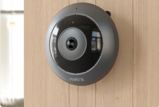 Kamera REOLINK Fisheye Series P520 Wewnętrzna, LAN / P2P, obiektyw, Wewnętrzna, precyzyjne, uruchamianie, Okrągła kamera Reolink zamontowana na drewnianej ścianie, widoczne odbicia światła i wnętrza pomieszczenia.