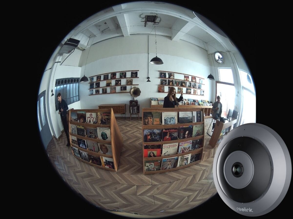 Kamera REOLINK Fisheye Series P520 Wewnętrzna, LAN / P2P, trzy tryby, podwójny, panoramiczny, cylindryczny, Obraz z kamery typu rybie oko Reolink, pokazujący wnętrze sklepu muzycznego z osobami przeglądającymi winyle; w prawym dolnym rogu widoczna kamera.