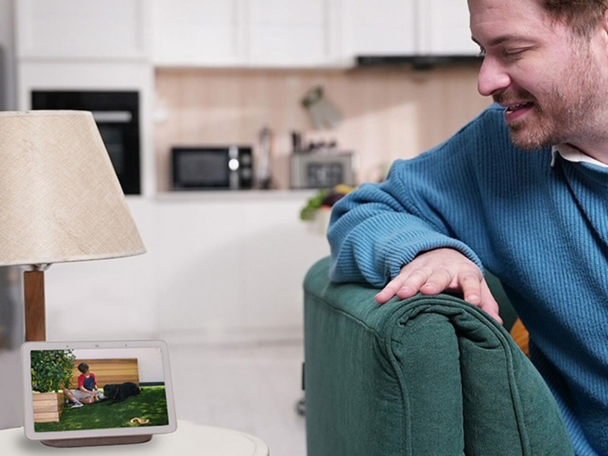 Kamera REOLINK Fisheye Series P520 Wewnętrzna, LAN / P2P, wykrycie, zaawansowane, obraz, nieistotne, Mężczyzna siedzi na sofie w jasnym salonie i patrzy na tablet stojący na stoliku, na ekranie wyświetla się podgląd z kamery monitoringu.