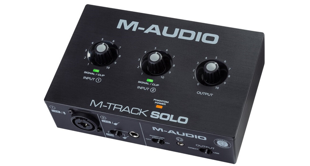 Czarny interfejs audio z trzema pokrętłami oznaczonymi jako INPUT 1, INPUT 2 i OUTPUT oraz napisami \'M-AUDIO\' i \'M-TRACK SOLO\'. Widoczne są wskaźniki SIGNAL/CLIP i przycisk PHANTOM POWER.
