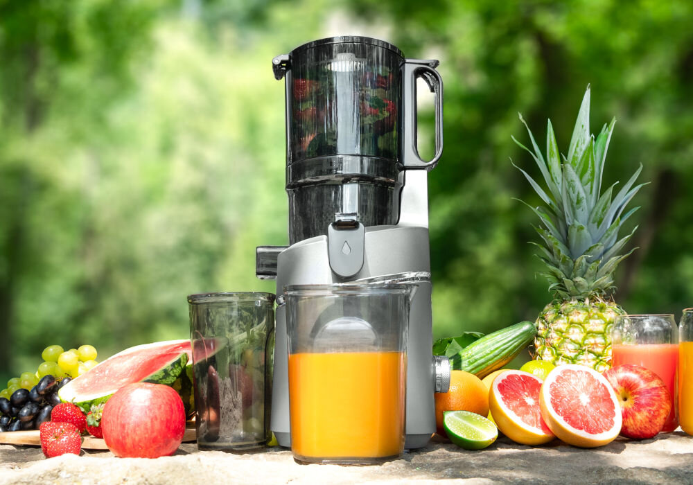 Wyciskarka wolnoobrotowa CONCEPT Juicy LO7120 Czarno-grafitowy z dwoma pojemnikami na tle roślin obok owoce blokada bezpieczeństwa bezpieczna praca bezpieczne wyciskanie soku