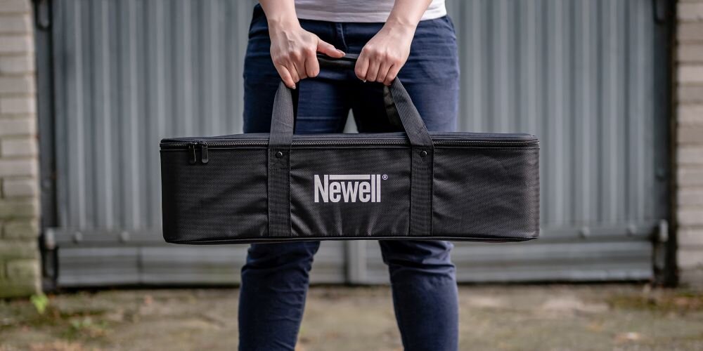 Osoba trzyma czarną torbę z napisem \'Newell\' na tle metalowych drzwi.