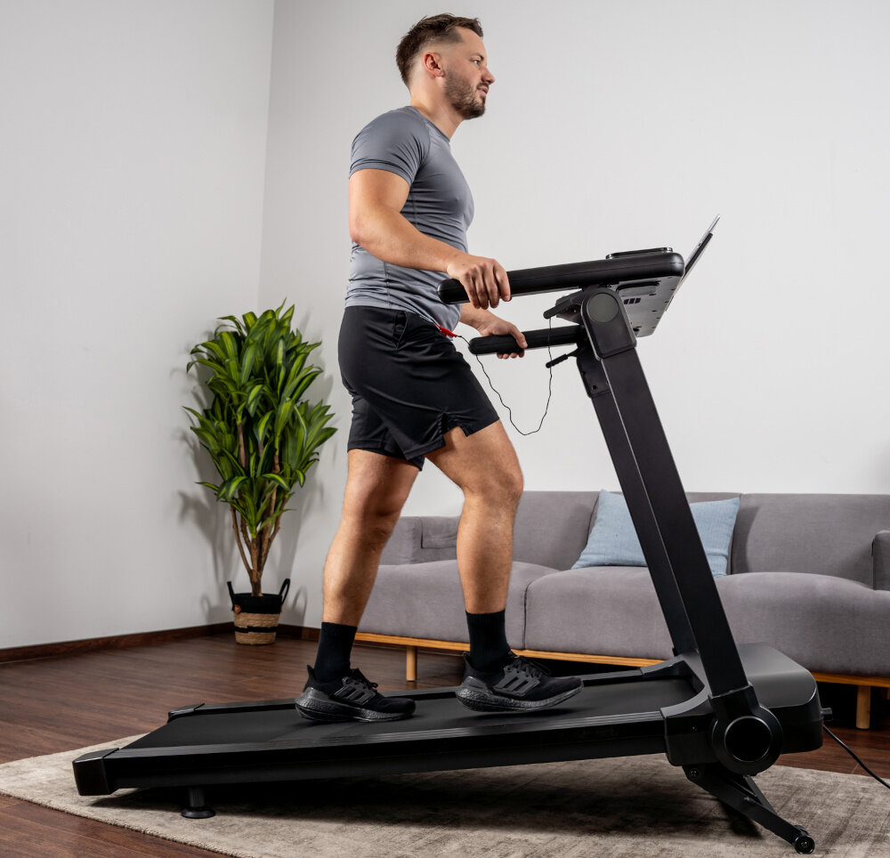 Bieżnia elektryczna KETTLER Track 200 1471W 16 km-h  dom pokój salon osoba idzie na bieżni w tle ściana aktywność w domu zdrowie codzienny trening automatyczna regulacja nachylenia 0-12% z 15 poziomami (co ok. 0,8%) można symulować biegi pod górkę zmienny kąt nachylenia urozmaica codzienne ćwiczenia