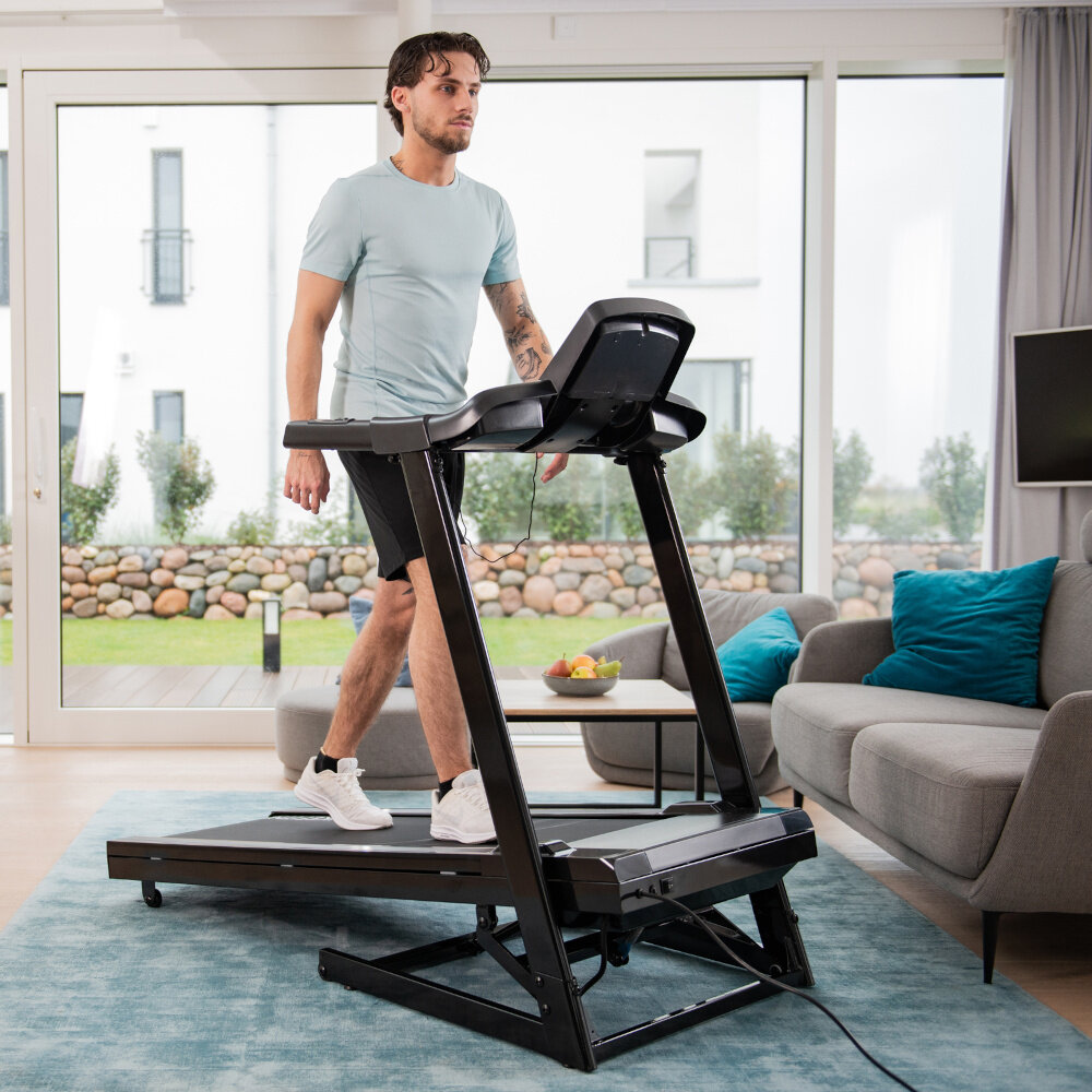 Bieżnia elektryczna KETTLER Track 100 1287W 16 km-h dom pokój salon osoba idzie na bieżni w tle okno za oknem ogród aktywność w domu zdrowie codzienny trening 