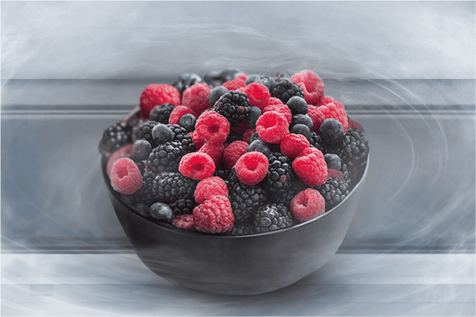 Zdjęcie przedstawia miskę z mrożonymi malinami stojącą na półce lodówki które otacza lodowa bryza 