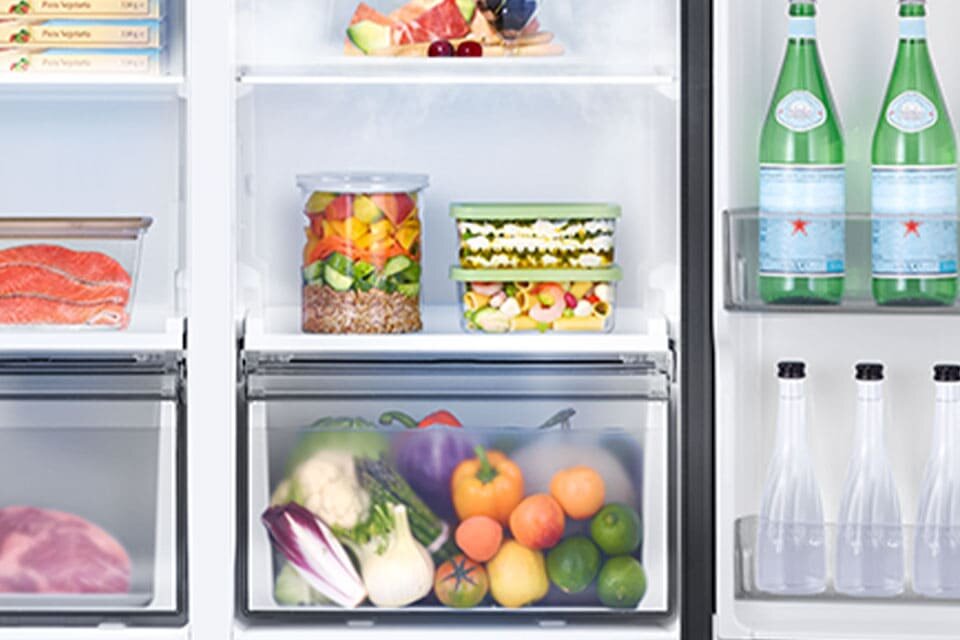 Zdjęcie przedstawia dwie szuflade lodówki z warzywami oraz półki na drzwiach lodówki na których stoją napoje