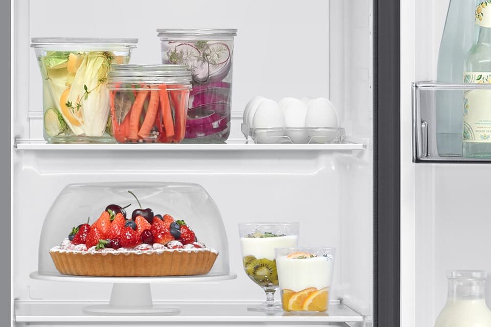 Na grafice dwie półki, na górnej półce stoją przetwory w słoikach i jajka, a na dolnej półce znajdują się desery