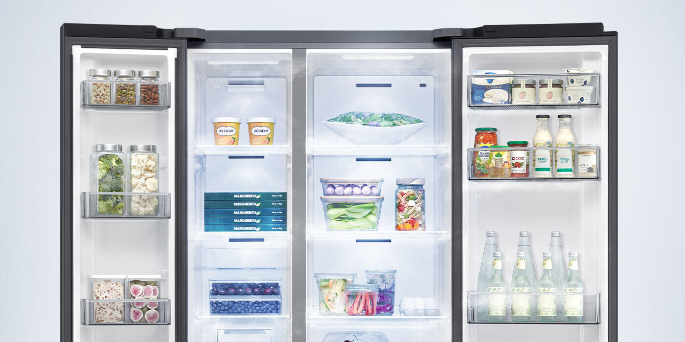 Otwarta lodówka z widocznymi półkami wypełnionymi różnorodnymi produktami spożywczymi, takimi jak warzywa, napoje i pojemniki z żywnością. Wewnątrz drzwi znajdują się dodatkowe półki z przyprawami i butelkami.