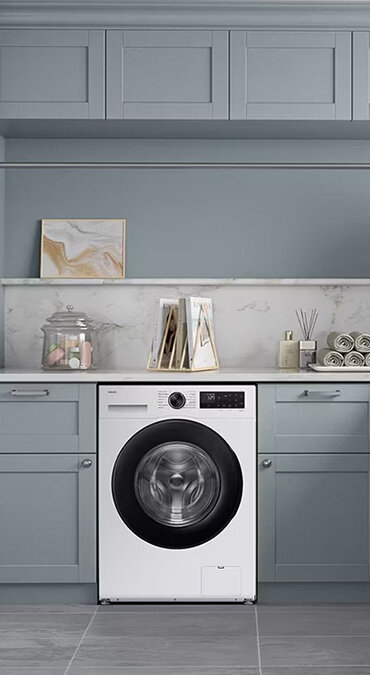 Pralka Samsung WW10FG5U34AEEO w eleganckiej pralni Pralka Samsung stojąca w zabudowie w eleganckiej pralni z szarymi szafkami, książkami, ręcznikami - dostępna w Media Expert