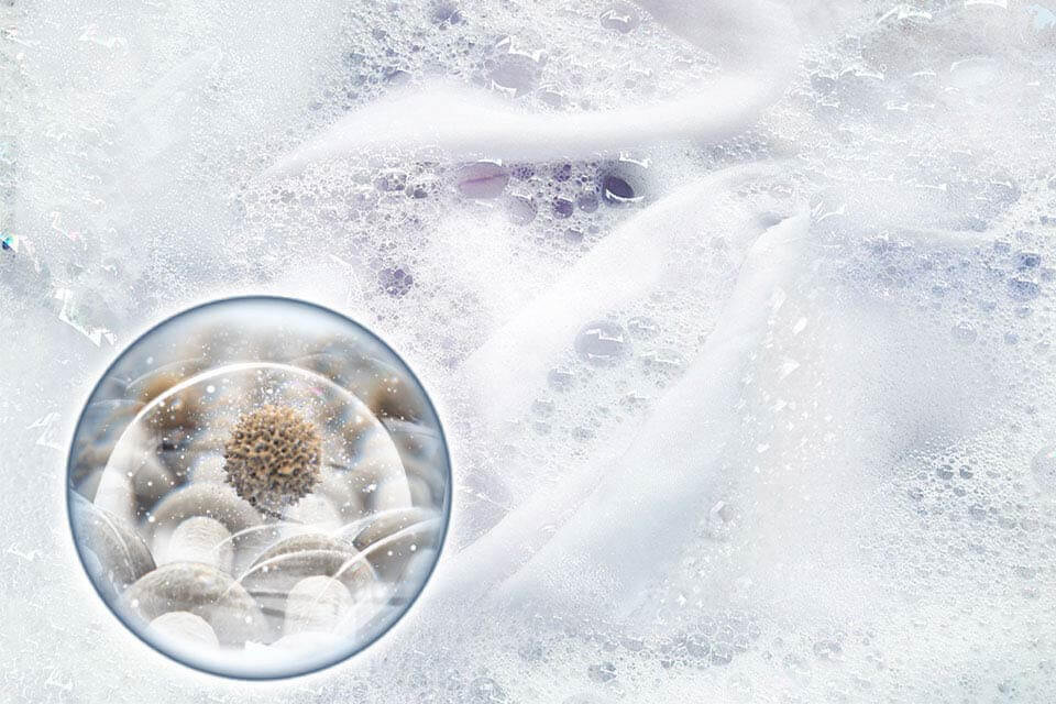 Zbliżenie na aktywną pianę z kapsułką detergentu i powiększeniem ukazującym usuwanie zabrudzeń na poziomie mikro.