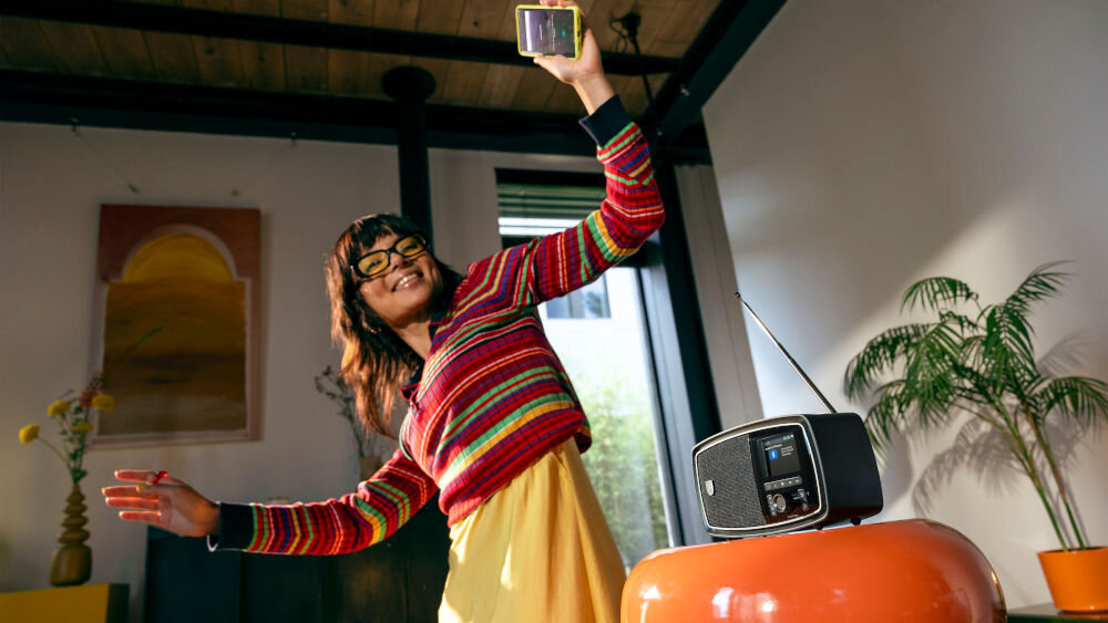 Radio PHILIPS TAV2000FB/00 tworzywo z recyklingu, certyfikat GRS, ekologiczne opakowanie, osoba z telefonem w ręku tańcząca w rytm muzyki