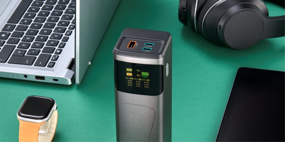 Powerbank Hama z wyświetlaczem LCD i portami USB-C oraz USB-A na biurku, otoczony laptopem, smartwatchem i tabletem.