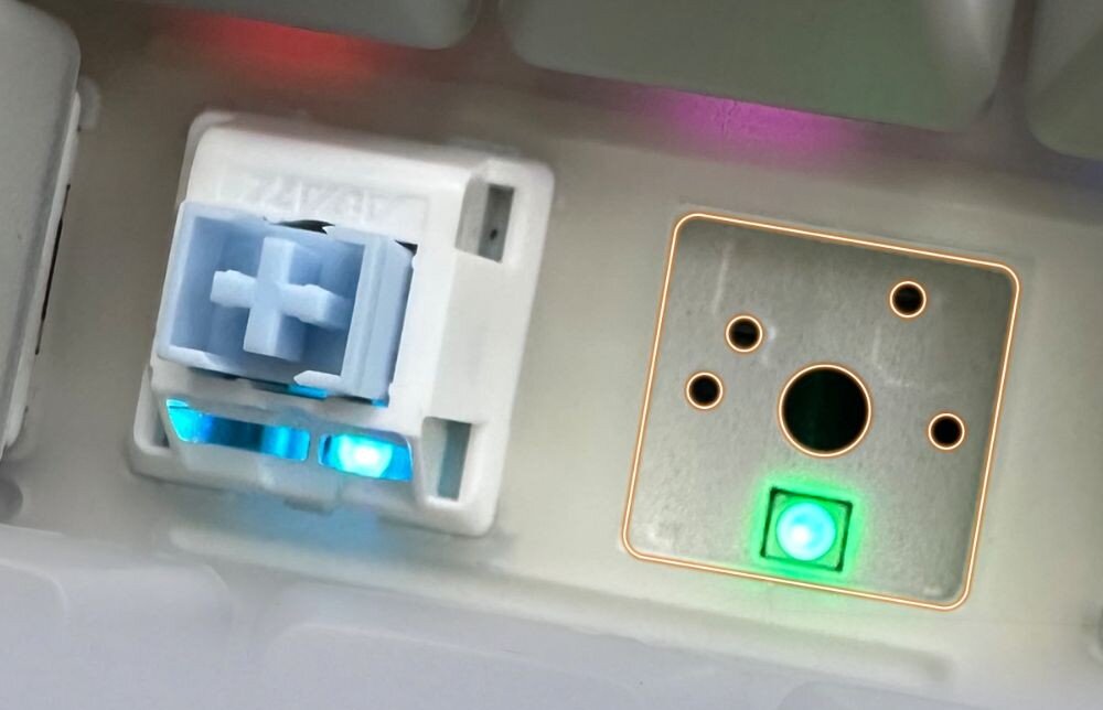 Klawiatura AJAZZ AK820 Pro RGB Zbliżenie na wnętrze klawiatury, gdzie widać zainstalowany przełącznik oraz puste gniazdo z widocznymi stykami podświetlone zielonym światłem, Hot-Swap, wymiana przełączników