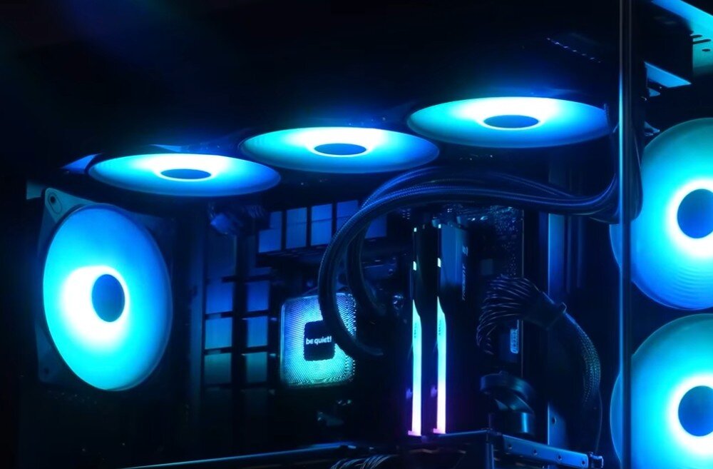 Chłodzenie CPU BE QUIET! Pure Loop 3 LX 360mm Wnętrze komputera z zamontowanym zestawem chłodzenia wodnego z trzema wentylatorami na górze obudowy i jednym z tyłu, wszystkie świecą niebieskim światłem, a blok chłodzący z logo na procesorze również jest podświetlony, opis
