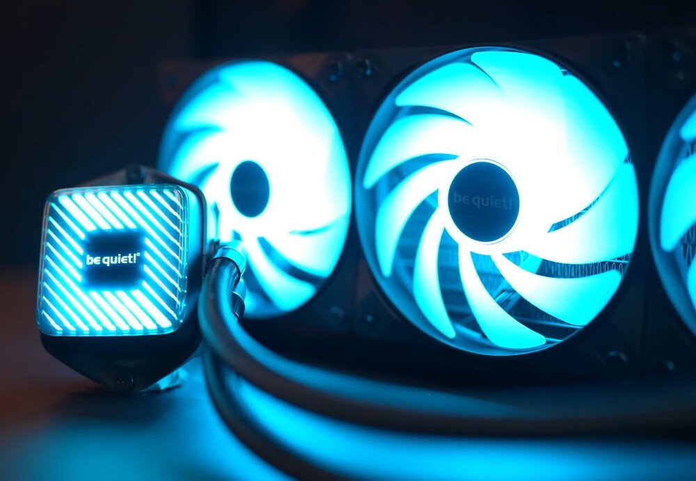 Chłodzenie CPU BE QUIET! Pure Loop 3 LX 360mm Zbliżenie na blok chłodzący i trzy wentylatory świecące niebieskim światłem, połączone przewodami w oplocie, ustawione na ciemnym tle, radiator, działanie