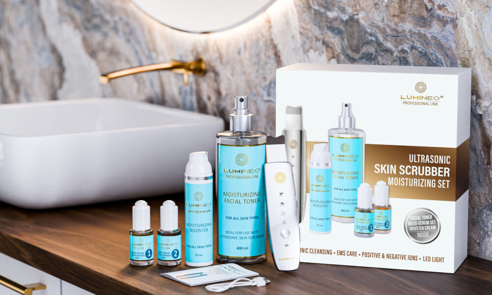 Urządzenie do peelingu kawitacyjnego LUMINEO M22 5w1 + Zestaw nawilżający (Tonik, 2 x Serum, Krem) Zestaw ULTRASONIC SKIN SCRUBBER MOISTURIZING SET od LUMNEO. Na drewnianej półce w łazience, na tle marmurowej ściany, widoczne jest białe pudełko zestawu oraz jego zawartość wyjęta obok: urządzenie do peelingu kawitacyjnego, butelka Nawilżającego Toniku Do Twarzy (400 ml), butelka Nawilżającego Boostera (75 ml), dwie małe ampułki MEZO-SERUM oraz kabel ładujący. Zestaw jest gotowy do użycia.