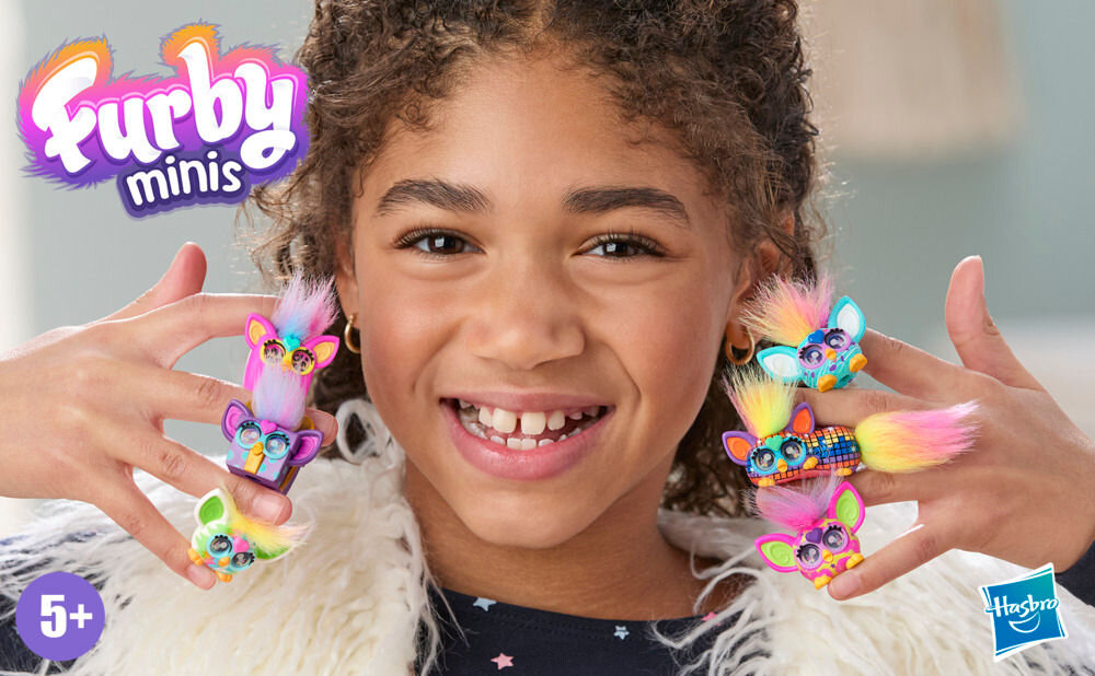 Zestaw figurek HASBRO Furby Minis G19515L0 Uśmiechnięta dziewczynka z kręconymi włosami prezentuje sześć różnych figurek Furby Minis umieszczonych na palcach dłoni, z logiem Furby Minis i Hasbro w rogach.