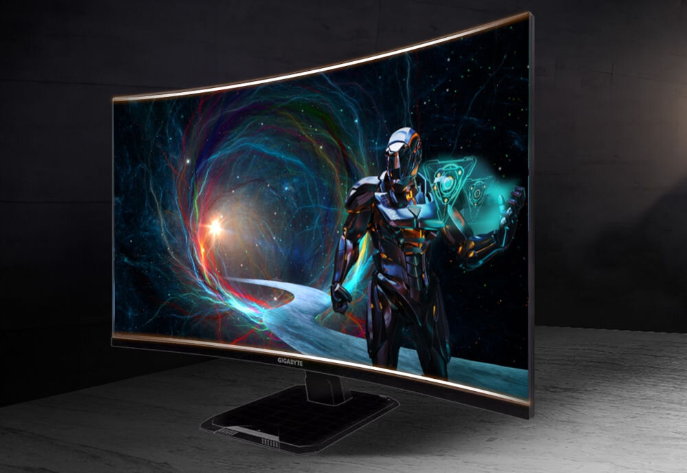 Monitor GIGABYTE GS32QCA 31.5 cala 2560x1440px 180Hz 1 ms [MPRT] Curved prezentacja monitora na biurku w pokoju o ciemnych ścianach na ekranie robot i galaktyczne tło zakrzywiony ekran QHD 2560 x 1440 px wysoka częstotliwość odświeżania niski czas reakcji szeroka paleta barw technologie redukujące migotanie filtrowanie światła niebieskiego ochrona wzroku