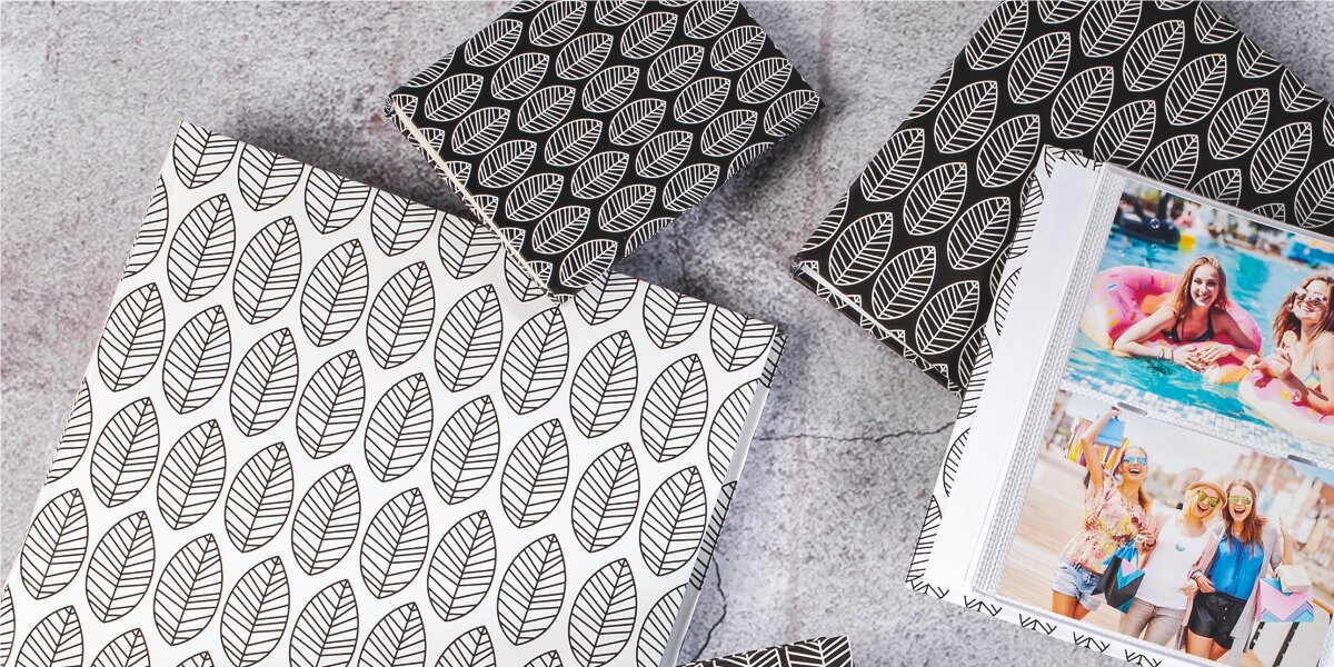 Stylowy album na wspomnienia Kilka albumów na zdjęcia z geometrycznym wzorem liści, w kolorystyce czarno-białej i biało-czarnej. Jeden album jest otwarty, pokazując zdjęcia z wakacji w kieszeniach foliowych.