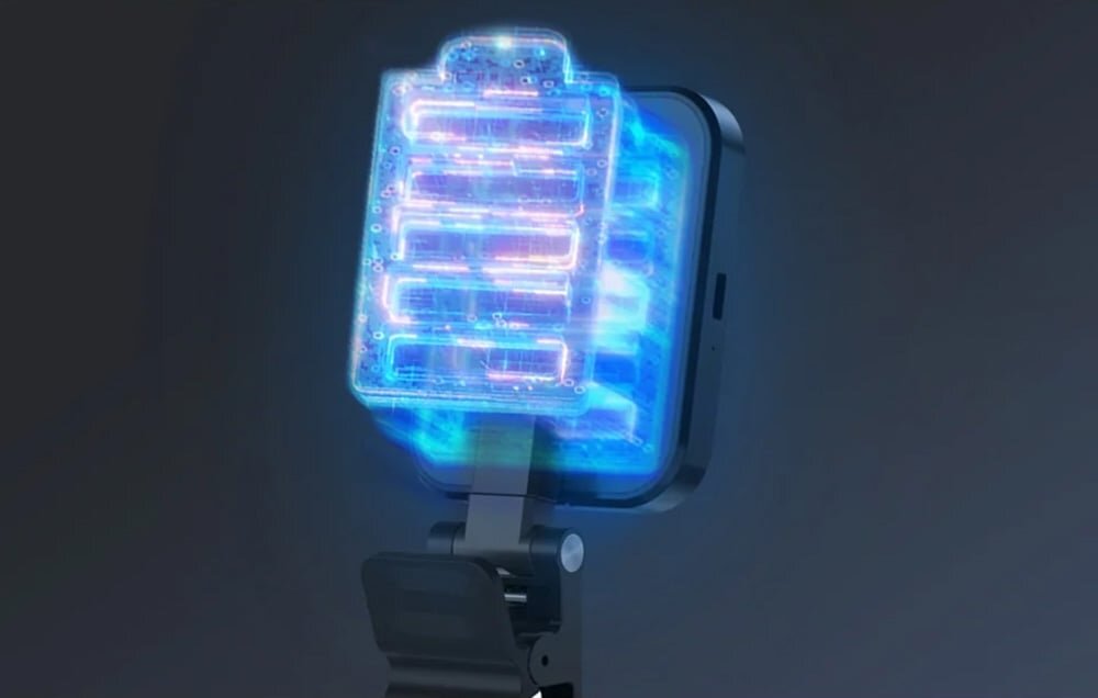Lampa LED o kwadratowym kształcie z widocznymi niebieskimi i różowymi światłami, zamontowana na uchwycie. Tło jest ciemne, co podkreśla jasność lampy.