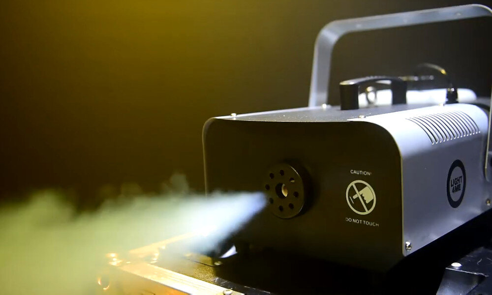 Wytwornica dymu emituje strumień białego dymu. Na urządzeniu widoczne są napisy: \'CAUTION DO NOT TOUCH\' oraz logo \'LIGHT4ME\'.