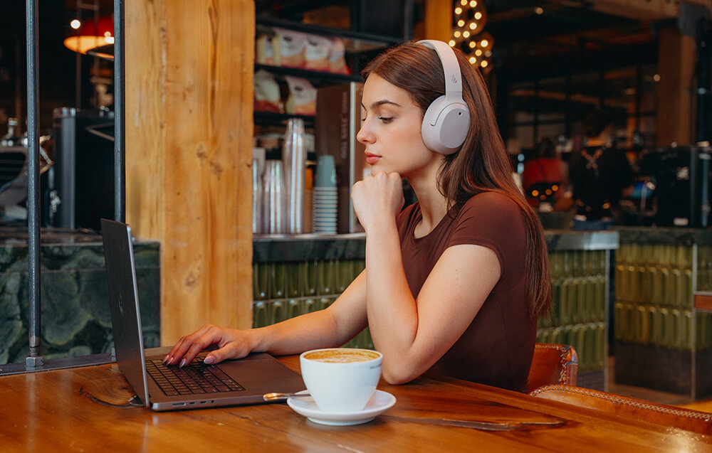 Edifier W820NB Plus V25 aplikacja ConneX Volume Guard przyciski diody sterowanie EQ, osoba z założonymi słuchawkami nausznymi w pomieszczeniu