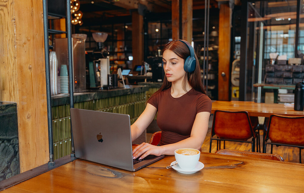 Edifier W820NB Plus V25 Bluetooth 6.1 Multipoint tryb Gaming niskie opóźnienie, osoba z założonymi słuchawkami nausznymi siedząca przed laptopem