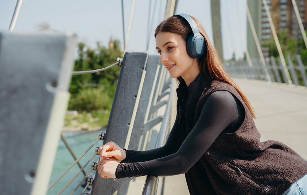 Edifier W820NB Plus V25 mikrofony AI redukcja szumów czysty głos rozmowy telefoniczne wideokonferencje, osoba z założonymi słuchawkami nausznymi w plenerze