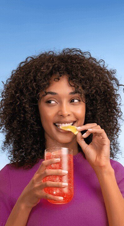 Dwie osoby wznoszą toast kieliszkami z gazowanymi napojami, jeden z plasterkiem brzoskwini, drugi z cytryną, na jasnym tle.