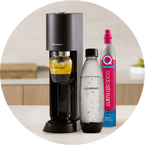 Maszyna SodaStream z czarną obudową, butelką z żółtym napojem i butelką wody gazowanej, obok pojemnik Quick Connect 60L