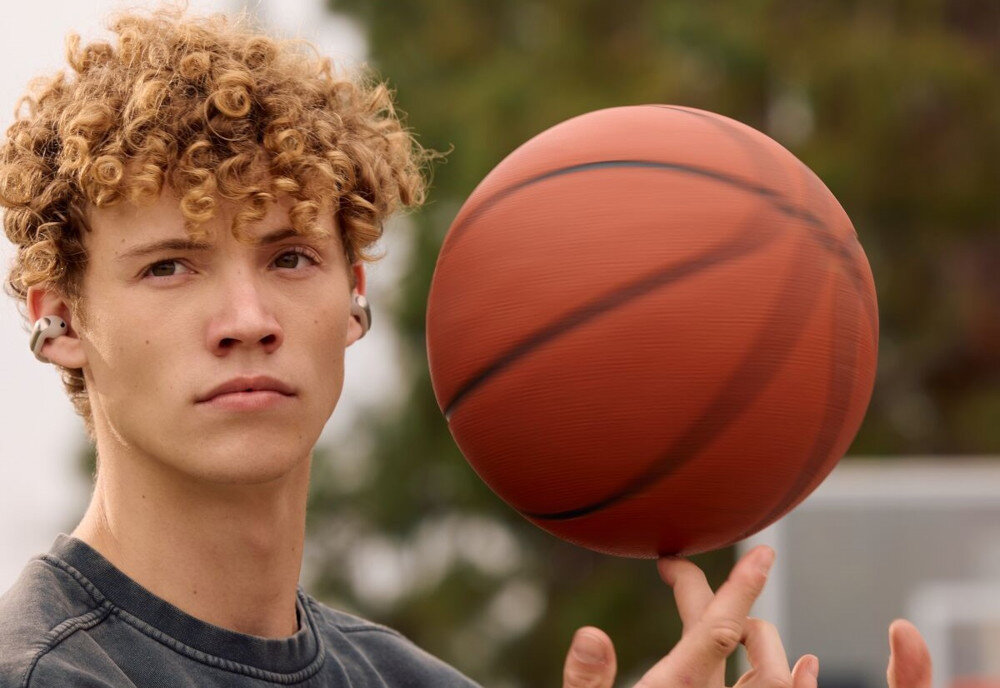 Słuchawki powietrzne BOSE Ultra Open przyciski sterowania i automatyczna zmiana głośności, osoba z założonymi słuchawkami powietrznymi kręcąca piłką