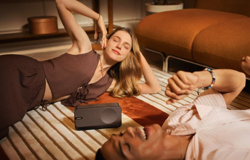 Głośnik mobilny BOSE SoundLink Home - połączenie stereo, dwa głośniki, szerokie brzmienie przestrzenne, osoby leżące na dywanie, słuchające muzyki wydobywającej się z głośnika