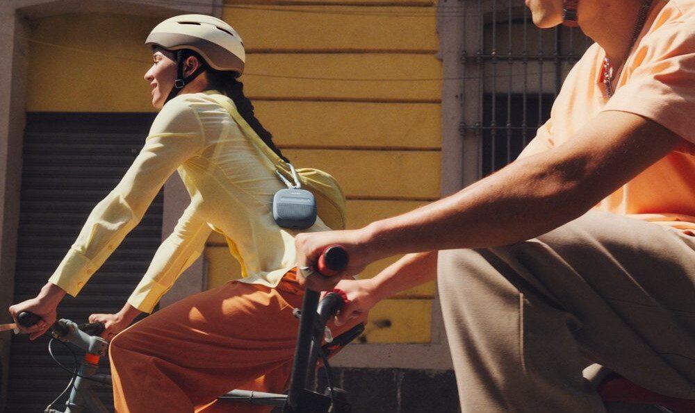 Głośnik mobilny BOSE SoundLink Micro 2nd Gen wodoodporny i odporny na kurz IP67 wytrzymała konstrukcja silikonowa, osoba jadąca na rowerze z przewieszonym na ramieniu głośnikiem 