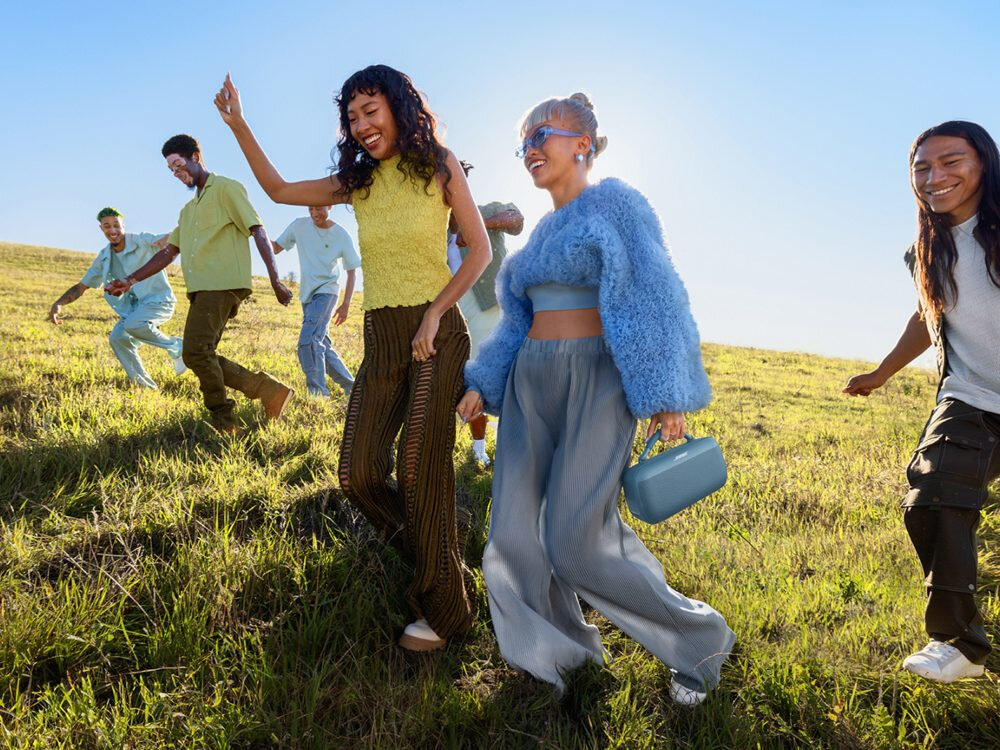 BOSE SoundLink Max przenośny uchwyt łatwe przenoszenie, osoby idące po polanie, osoba trzymająca głośnik w ręku