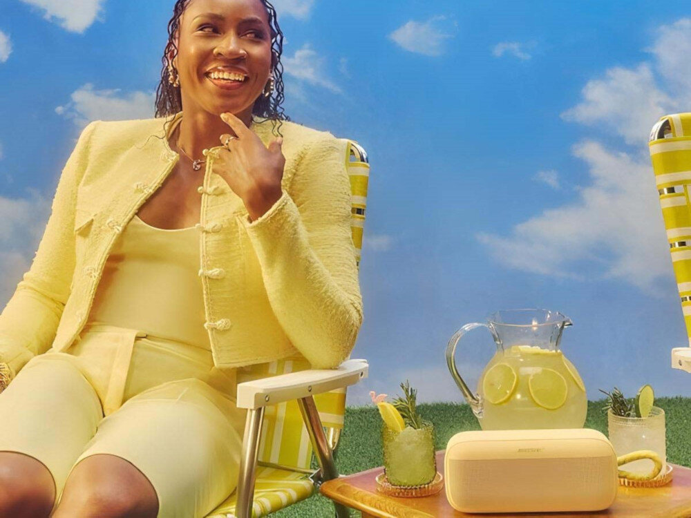 Głośnik mobilny BOSE SoundLink Plus wodoodporny IP67 odporny na kurz i wstrząsy, osoba siedzaca na krześle przy stoliku, głośnik stojący na stoliku