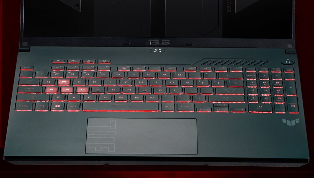 Laptop z podświetlaną na czerwono klawiaturą, widoczne logo ASUS nad klawiaturą oraz logo TUF na obudowie. Na touchpadzie znajduje się napis \'TUF\'.